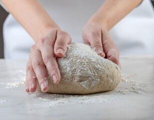 Close-up of hands kneading dough, covered in flour, on a white surface, preparing for baking.
