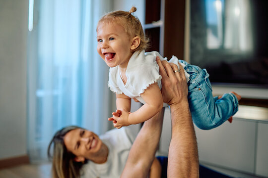 Cheerful toddler girl playing with her parents indoors, father lifting her up, mother smiling in the background. Capturing family bonding
