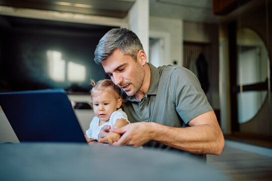 Dad and baby girl sharing special moments, exploring online content on a laptop, fostering early learning and family connection