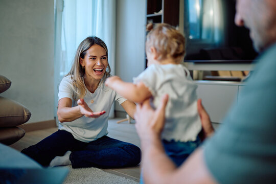 Happy family spending time together, mother smiling and encouraging toddler while father supports learning to walk