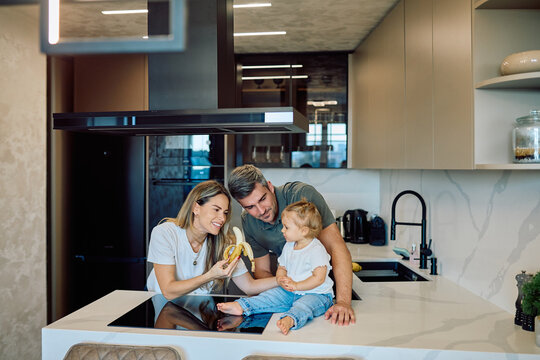 Parents and toddler enjoying a banana together in a bright, contemporary kitchen, sharing a moment of family bonding