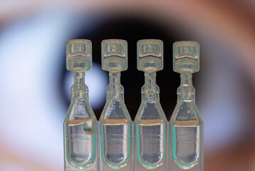 A row of single-dose artificial tear vials focused in the foreground with a blurred human eye in the background.