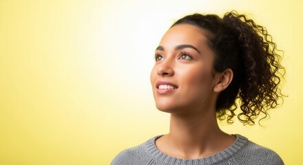 A young woman with curly hair gazes upwards against a bright yellow background, conveying a sense of hope and contemplation.