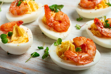Boiled eggs stuffed with yolk and seasoned with mayonnaise, stuffed eggs with shrimp, on a white wooden chopping board, selective focus, close-up, without people,