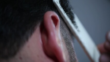 A professional barber uses sharp scissors and a comb for precise hair trimming around the ear. Close-up detail of the salon cutting process.