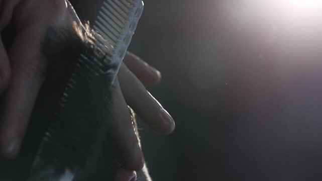A professional barber uses sharp scissors and a comb for precise hair trimming around the ear. Close-up detail of the salon cutting process.