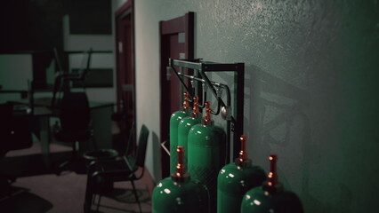In a dimly lit room, a row of green gas cylinders stands against the wall. Chairs are scattered nearby, suggesting an area for workers to gather before or after tasks. © icetray