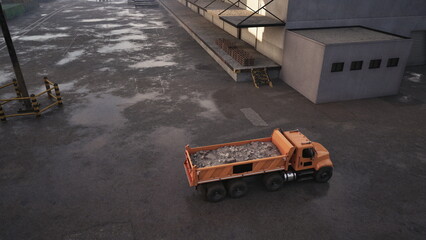Naklejka premium A vibrant orange dump truck stands at a construction site, unloading a pile of gravel. The ground is wet, reflecting early morning light, with a gray building in the background.