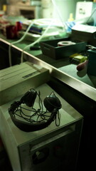 In a dimly lit room, old headphones rest on a table surrounded by various vintage tools and equipment, creating an eerie yet nostalgic atmosphere. The soft green light enhances the mysterious vibe.