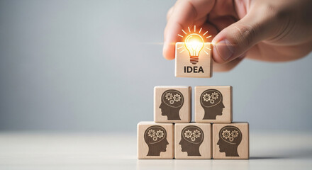 Hand putting wooden block with light bulb and idea text on top of human head blocks