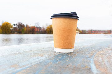 Closeup front view single brown paper coffee cup in peaceful outdoor scene with autumn trees