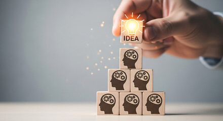 Hand placing idea cube on top of pyramid of head cubes, symbolizing creative thinking