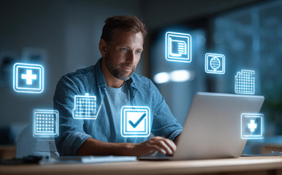 Focused man using laptop for online health insurance and digital healthcare. Hologram icons show virtual access to medical service, telemedicine, and claim approval