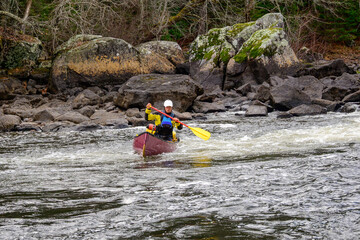 Experiential education: a young man solo paddling a red canoe in moving water (rapid) on the Madawaska River on a late fall afternoon room for text