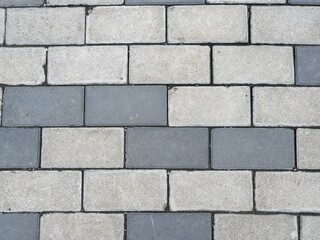 Top down, close up view of a modern pavement surface created with interlocking rectangular concrete paving blocks in a repeating pattern of light and dark gray.