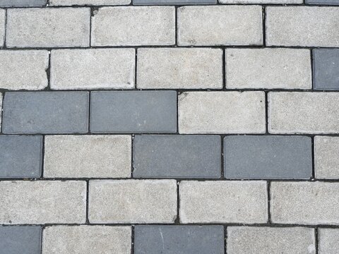 Top down, close up view of a modern pavement surface created with interlocking rectangular concrete paving blocks in a repeating pattern of light and dark gray.