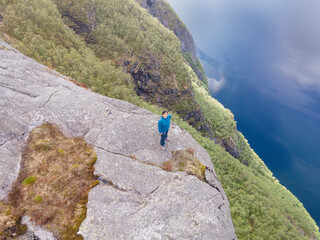 Naklejka premium Woman standing on mountain cliff above Ørsdalsvatnet lake in Norway, aerial drone view