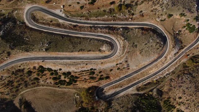 Aerial view of S-shaped asphalt roads winding down mountainous terrain. Travel, transportation, and challenging geography.