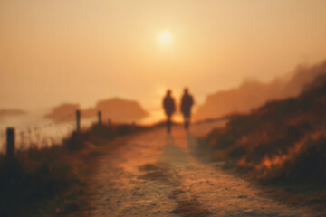 Blurred view of man and woman walking along coastal path at sunset