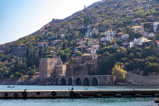 View of Alanya's historic peninsula with the medieval Seljuk shipyard in foreground and hilltop Ottoman houses with terracotta roofs leading to the fortress walls. Alanya, Turkey.


