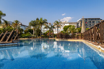 Blue-tiled fountain pool in Abdurrahman Alaettinoglu Park reflecting palm trees and Mediterranean architecture under sunny sky, creating refreshing resort atmosphere. Alanya, Turkey.

