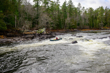 Adventure: a young man solo paddles down a rapid on the Madawaska river in a green canoe loaded with camping equipment room for text