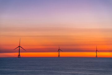 Witness a breathtaking summer sunset at Houlong Beach, Miaoli County, Taiwan. See the sun slowly descend behind wind turbines over the tranquil sea.