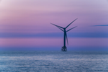 A spectacular twilight view of a stationary wind turbine and a freighter in the sea, set against...