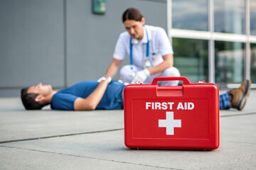 A gloved medic performs CPR on a man lying on the ground. A first aid kit is nearby