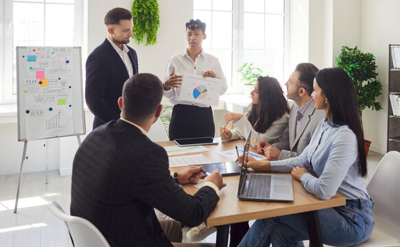 Business meeting of corporate company employees team for board presentation in office boardroom. Businesswoman pointing on report chart standing at desk with group of people. Expertise concept