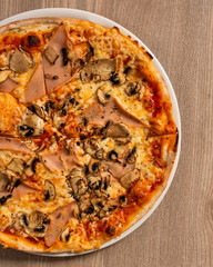 A top view of Pizza capricciosa with tomatoes, greens, mushrooms and cheese on a wooden table