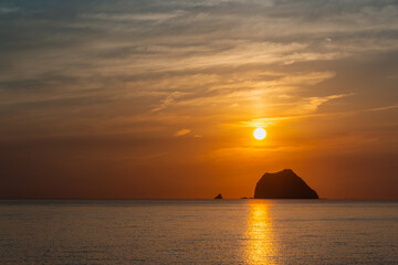 Experience a mysterious sunrise at Waishuangxi, Taiwan, with Keelung Islets, fishing boats, and a dreamy orange golden sky as sun peeks through clouds.