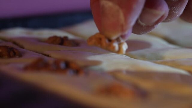 Close-up shot of a cook preparing homemade Baklava dessert. Raw diamond-cut dough sits in a baking pan. The chef places walnut pieces onto the pastry squares before baking.