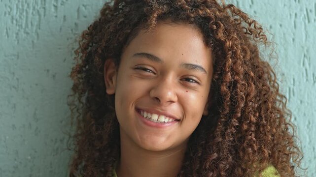 Smiling Girl With Curly Hair Leaning Against Textured Wall, Joyful Close Up Portrait Showing Teeth And Expressive Eyes In Relaxed Indoor Setting