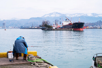 A fisherman fishes in the port of Batumi on a winter day in January.