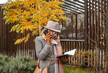 Fototapeta premium Blonde businesswoman enjoying outdoor conversations connecting with smartphone in a stylish autumn setting
