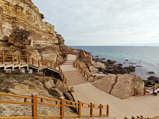 Coastal pathway features wooden boardwalk winding through rocky terrain by the ocean