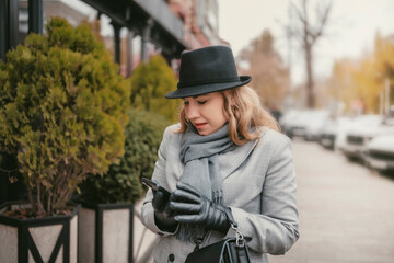 Fototapeta premium Blonde woman enjoying a cheerful autumn day on a city street using smartphone