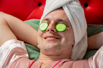 Cucumber slices under man eyes, Man wearing a bathrobe and towel on his head. Concept of facial skincare and self-care routine