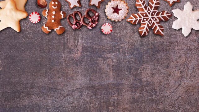Christmas sweets top border. Overhead view, stop motion loop video on a dark stone background with copy space. Gingerbread and an assortment of cookies.