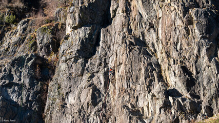 ock climber ascending steep limestone cliff face in mountain terrain