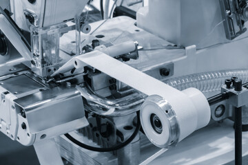 A sewing machine is in use. machine is white and has a clear cover.  machine is in the process of sewing a piece of fabric