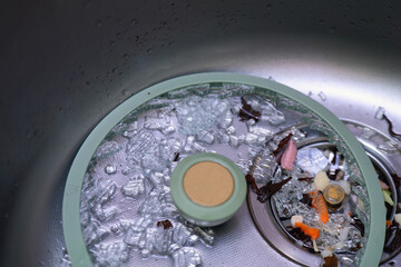 Shattered glass pot lid with silicone rim lies in kitchen sink, sharp shards pose cut risk
