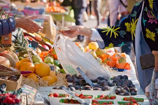 Client qui paye son achat de fruits et l&eacute;gumes frais sur un march&eacute; ensoleill&eacute; de Nice