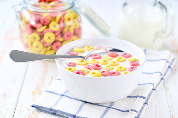 Making a healthy breakfast cereal using corn rings and strawberry rings and milk.