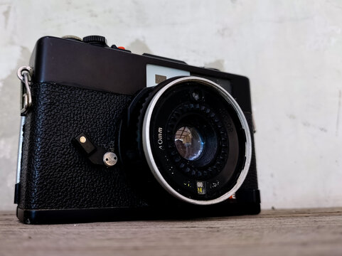 A vintage film camera with a black textured body details sits on a wooden surface. 