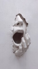 Sculpture of a face emerging from wall with a hand holding its mouth, symbolizing dramatic expression and emotion