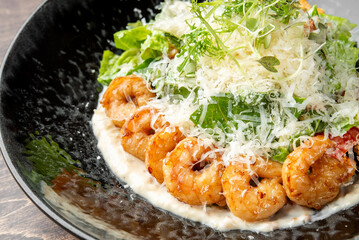 delicious Caesar salad topped with grilled shrimp, grated Parmesan cheese, and fresh greens, served on a black plate.
