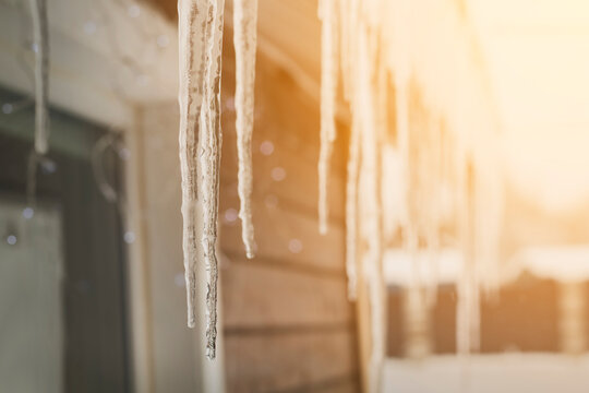 Sharp icicles hanging down from the roof of the residential building against sunny background. Transparent icicles on facade of building, dangerous icicles melt on rooftop, risk of injury