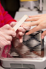 Manicure treatment. Spa therapy. Female beautician in gloves using emery board preparing female clients hands for nail beauty procedure.